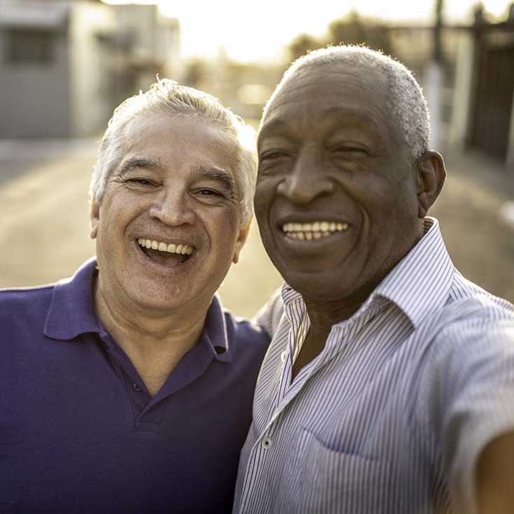 Two older men smile at the camera outdoors