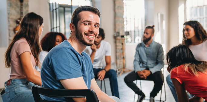 A man looks at the camera in the midst of a group therapy session